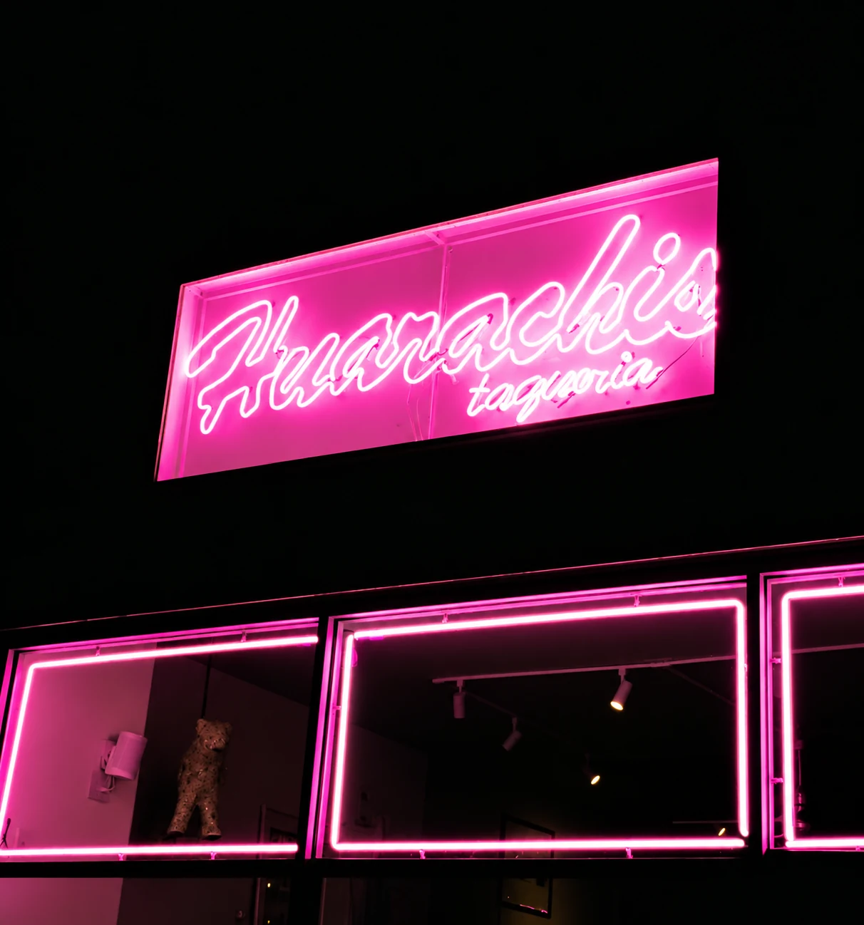 Pink neon Huarachis Taqueria sign and storefront at night